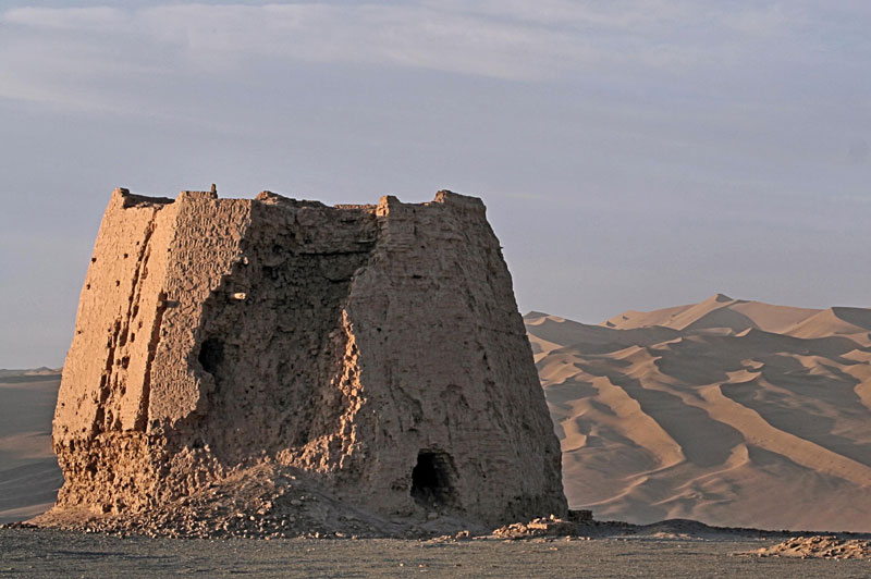 A Han dynasty-era rammed earth watchtower in Gansu province. The dunes of the Gobi desert stretch behind the ruins.