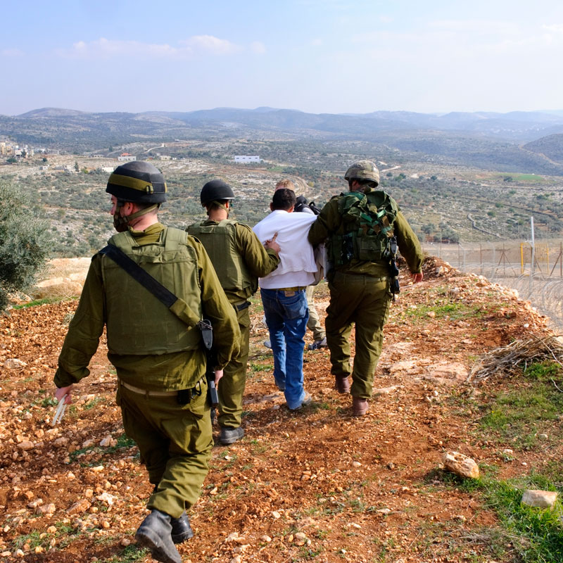 A group of soldiers are walking with a captured man in a white shirt.