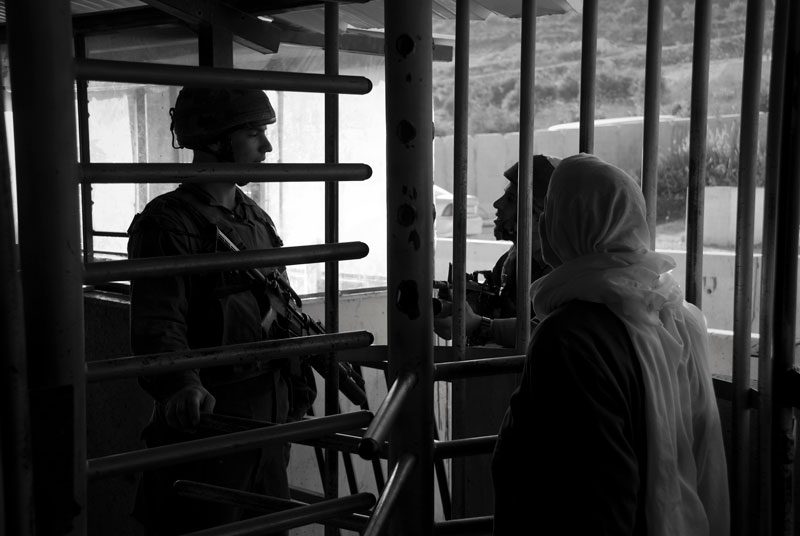 A woman speaking to two soldiers behind a metal fence.