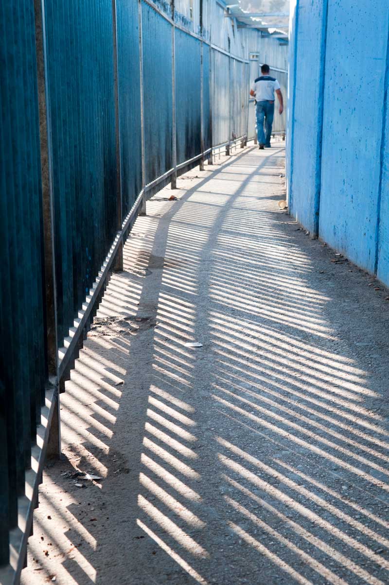 A man walking in a space between a metal fence and a concrete wall.