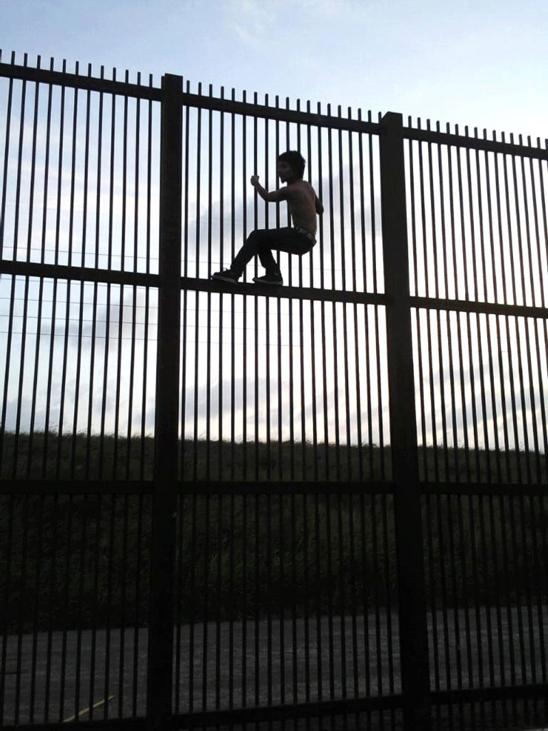 The silhouette of a young man scaling the US/Mexico border wall near Douglass, Arizona.