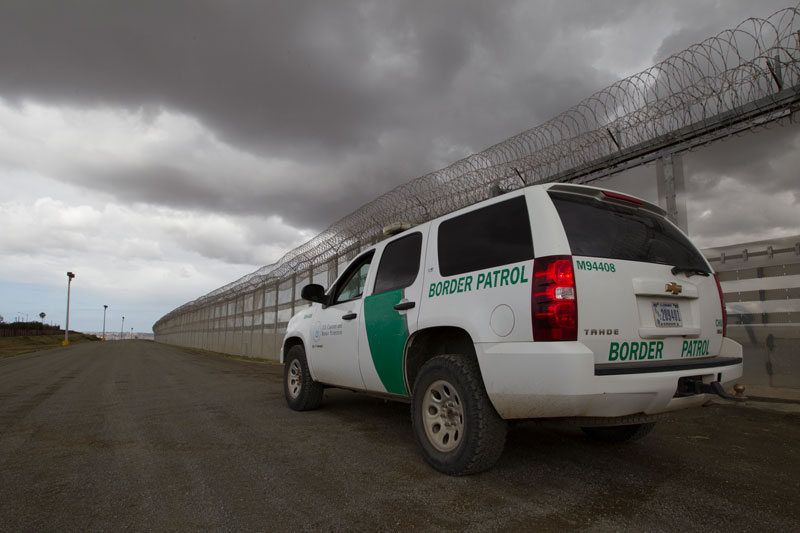A green and white border patrol vehicle parked in front of a wall.