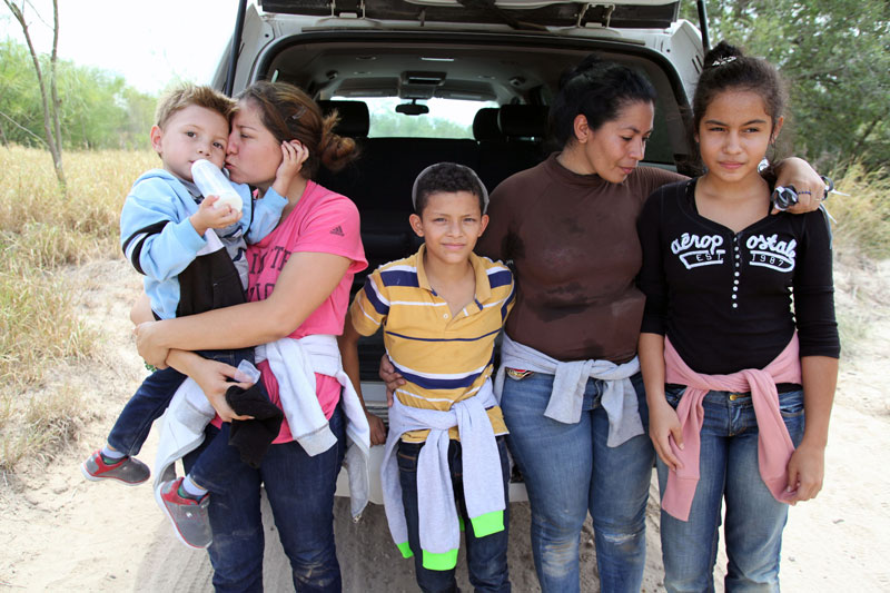 A family of five standing in front of their vehicle.