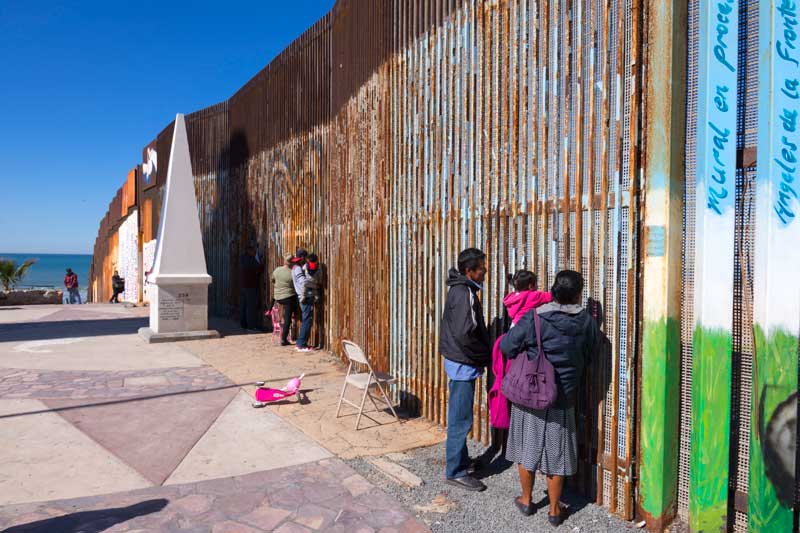 Family standing next to a large metal wall to talk to speak to family on the opposite side.