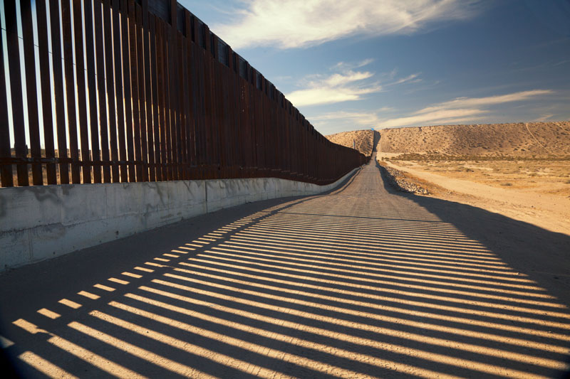 A view of a tall metal fence with the sun shining through.